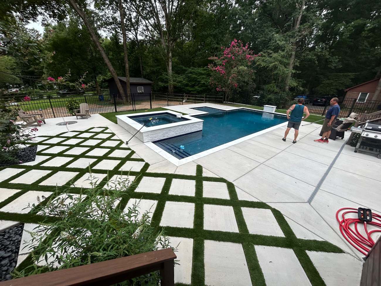Aerial view of a modern renovated pool with white stacked-stone spa and diamond turf-ribbon concrete deck