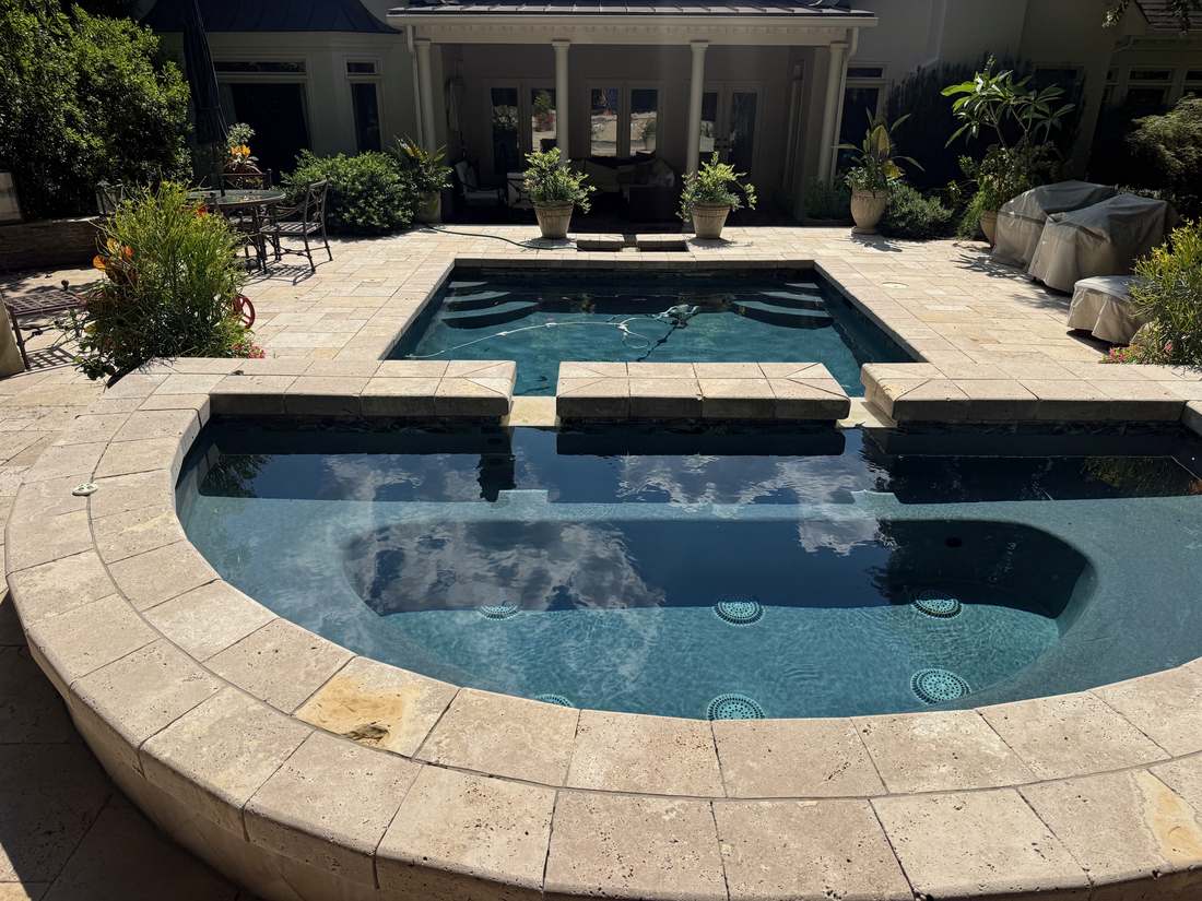 Round raised spa with square spillway basin in a travertine courtyard